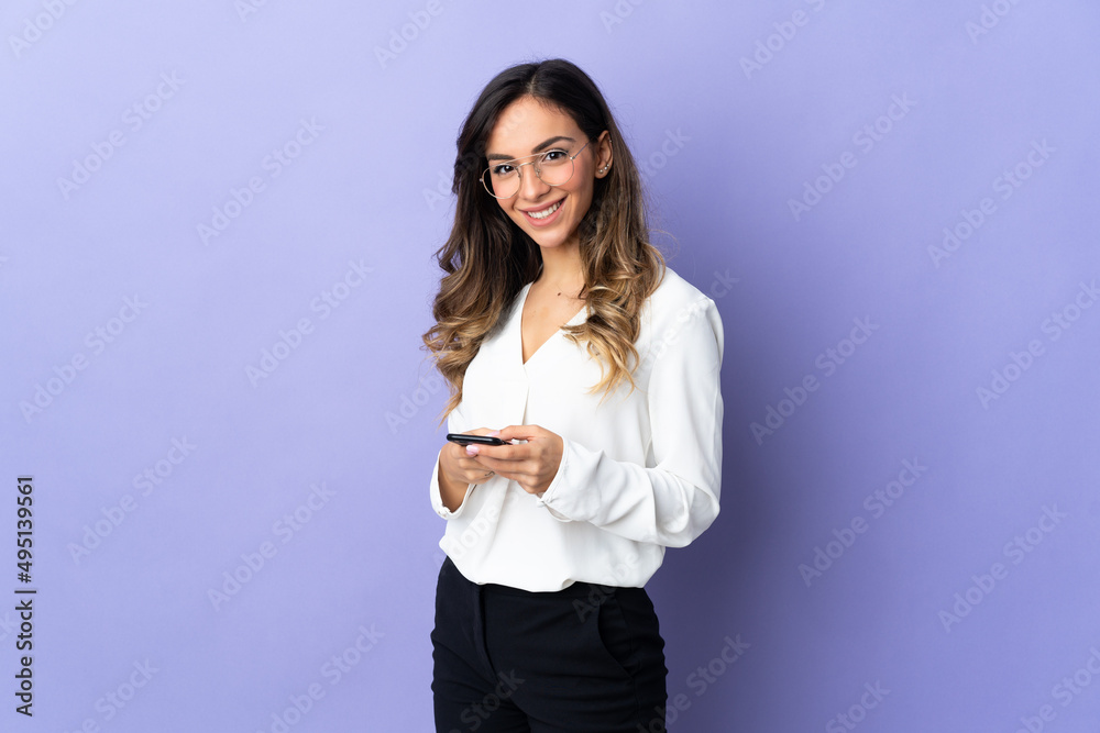 Young caucasian woman isolated on purple background sending a message with the mobile Young caucasian woman isolated on purple background sending a message with the mobile