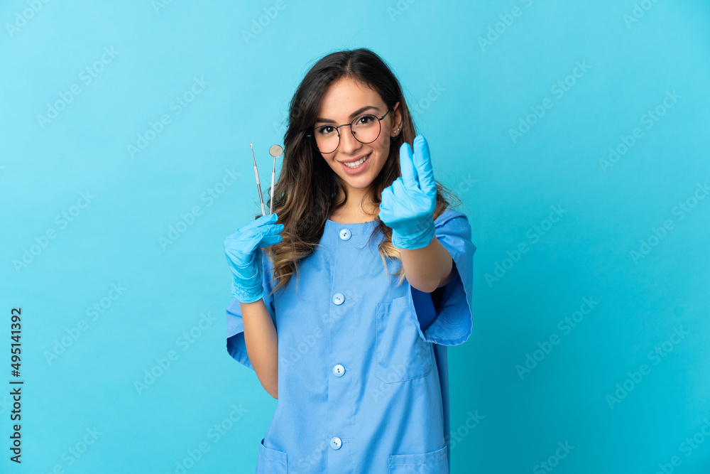 Woman dentist holding tools over isolated on blue background making money gesture Woman dentist holding tools over isolated on blue background making money gesture
