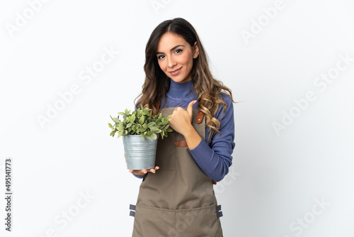 Gardener girl holding a plant isolated on white background giving a thumbs up gesture