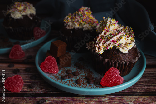 Tasty chocolate muffin cupcake with colourful sprinkles white cream topin, truffles and heart shaped candy for valentines day celebration photo