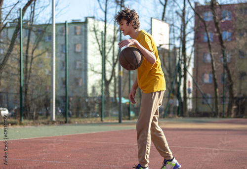 Cute young teenager in yellow t shirt with a ball plays basketball. Sports, hobby, active lifestyle for boys