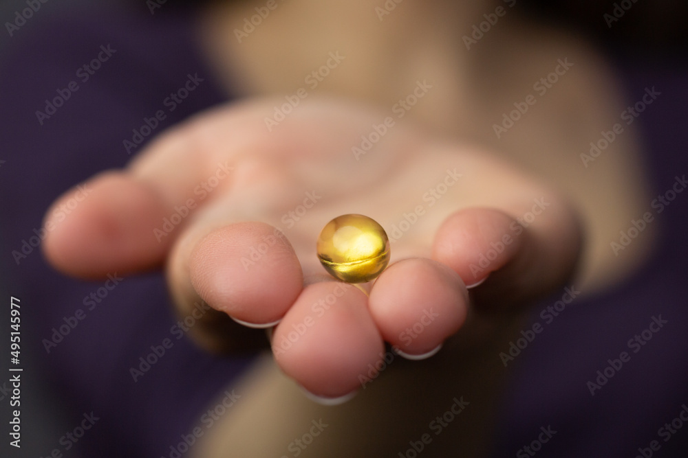 Closeup of a woman holding a fish oil capsule – source of vitamin D and omega 3 fatty acids.