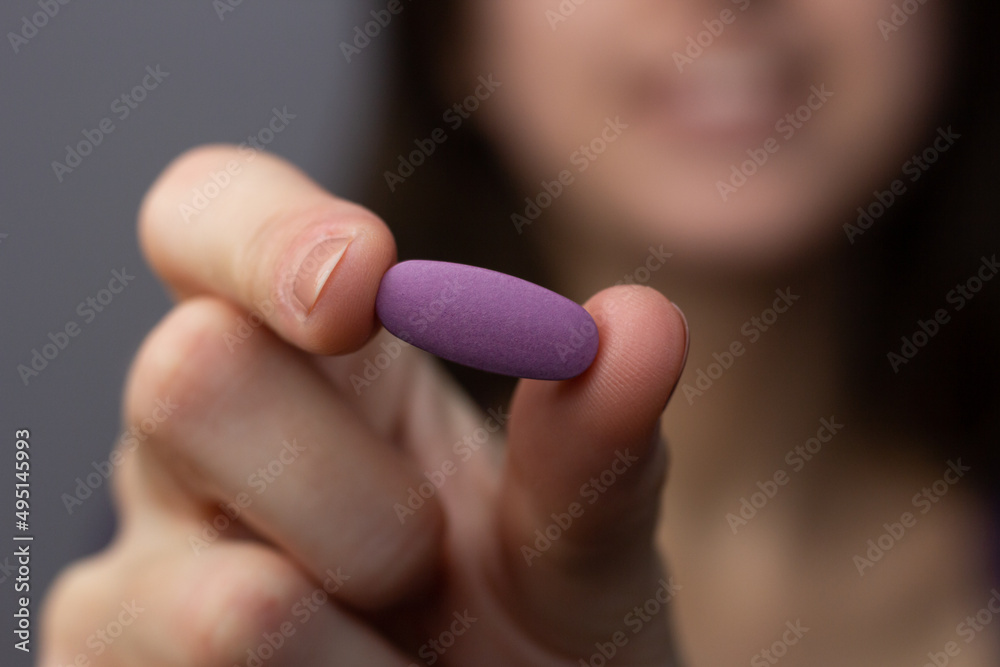 Closeup of a woman holding a purple multivitamin pill.