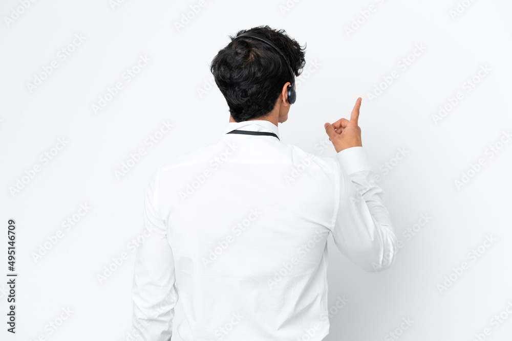 Telemarketer man working with a headset isolated on white background pointing back with the index finger Telemarketer man working with a headset isolated on white background pointing back with the index finger