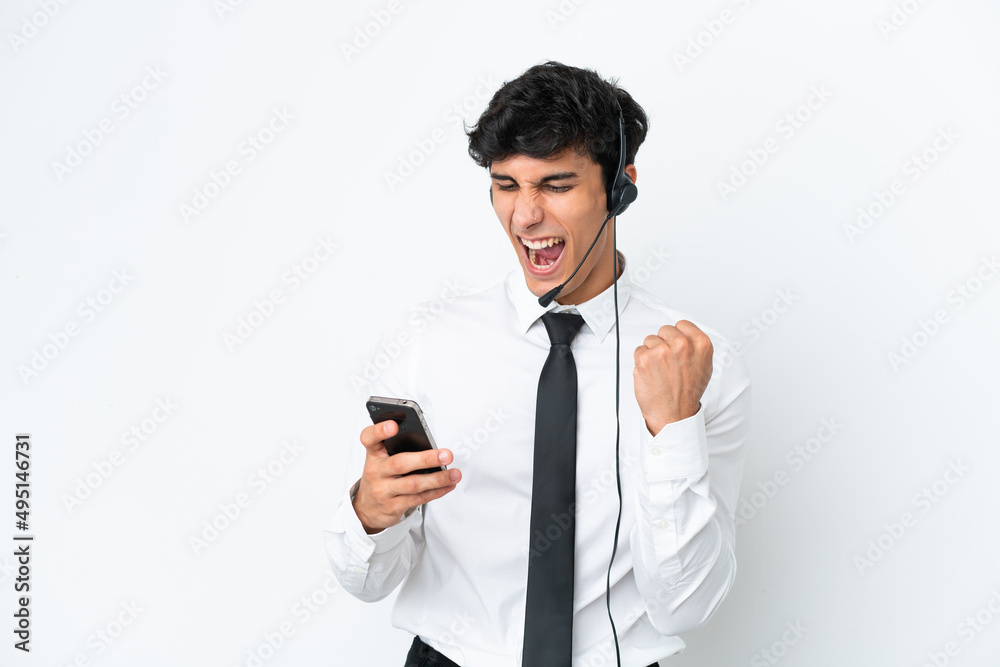 Telemarketer man working with a headset isolated on white background with phone in victory position