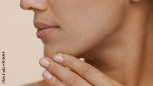 Extreme close-up shot of young woman with perfect skin strokes her jaw line and chin on beige background | Smooth skin and beauty care commercial concept