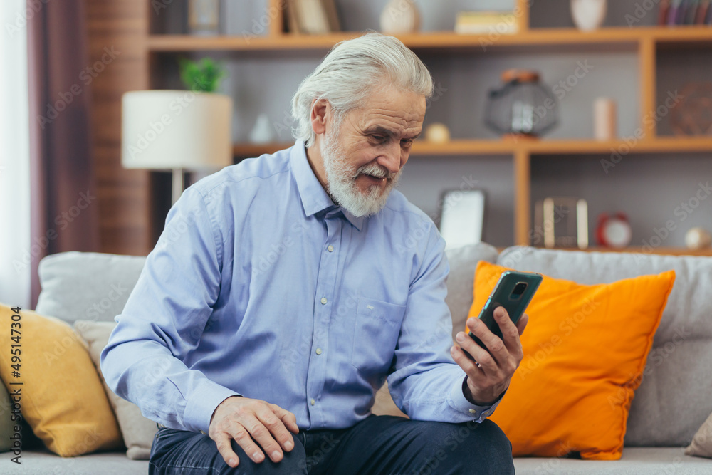 Senior man at home sitting on sofa looking at phone screen, talking on video call with family Senior man at home sitting on sofa looking at phone screen, talking on video call with family