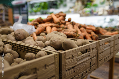 Soft focused shot of fresh potatoes and carrots in boxes in grocery department store, supermarket, local shop. Organic food
