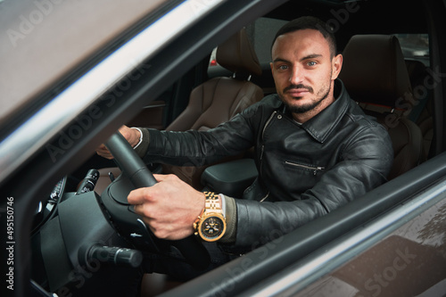 Portrait of handsome young man driving modern car. Guy wearing casual clothes and gold watch.