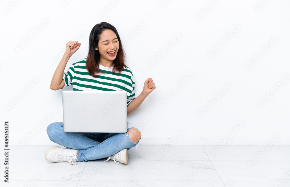 Young Vietnamese woman with a laptop sitting on the floor isolated on white wall celebrating a victory Young Vietnamese woman with a laptop sitting on the floor isolated on white wall celebrating a victory