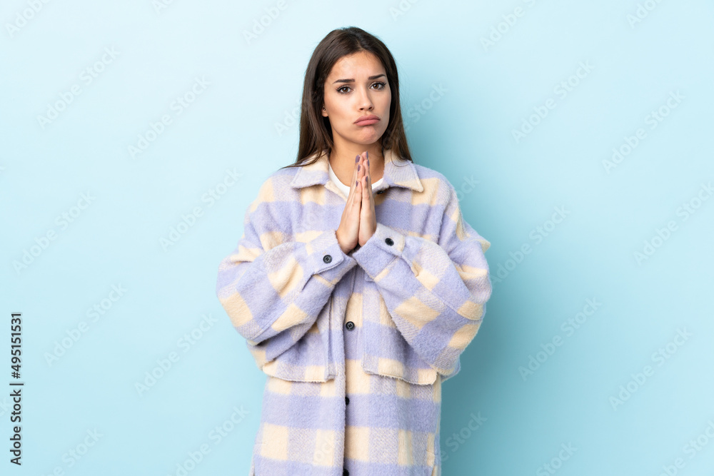 Young caucasian woman isolated on blue background keeps palm together. Person asks for something Young caucasian woman isolated on blue background keeps palm together. Person asks for something