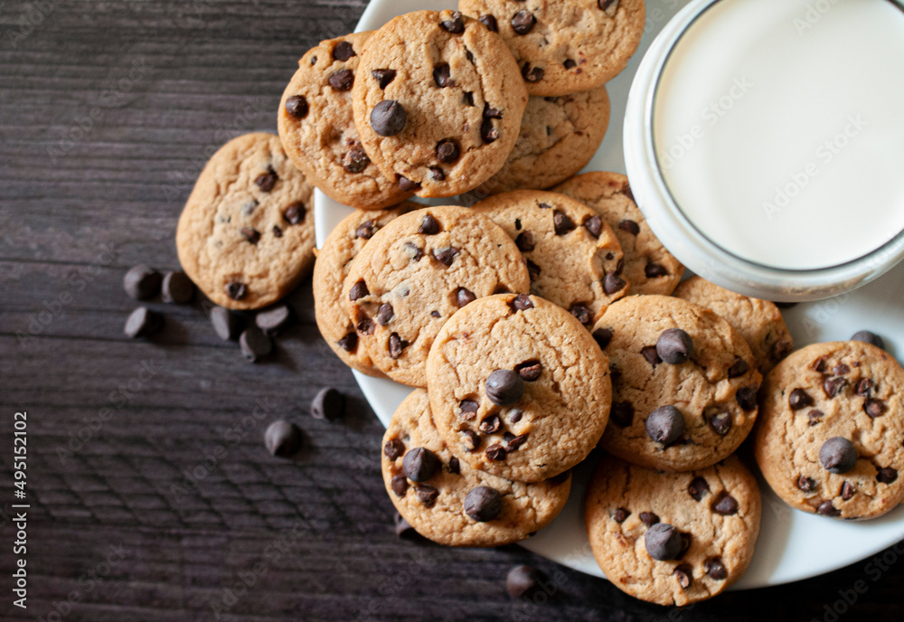 Chocolate chip cookies on a white plate, with a cold glass of milk on the side, over a wooden table. Chocolate chip cookies on a white plate, with a cold glass of milk on the side, over a wooden table.