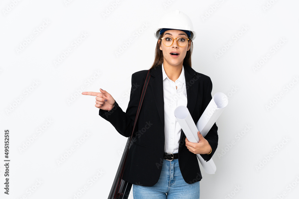Young architect caucasian woman with helmet and holding blueprints over isolated background surprised and pointing finger to the side Young architect caucasian woman with helmet and holding blueprints over isolated background surprised and pointing finger to the side