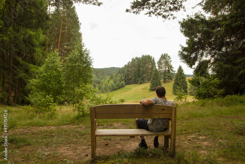 Mann auf Bank im Wald von hinten mit Blick auf Wald, Bäume, Hügel im Urlaub