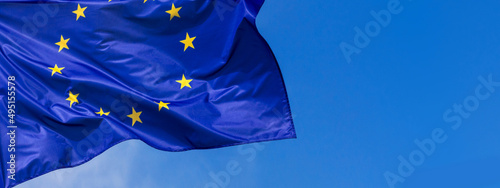 Flag of the European Union waving in the wind on flagpole against the sky with clouds on sunny day, banner, close-up