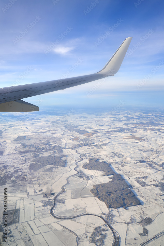 Flying and traveling. View from airplane window on the wing during sunset. Plane over land in winter.
