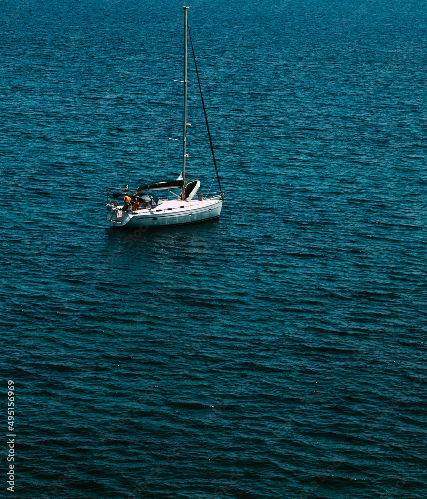 Fototapeta premium Sailing boat anchored in the clear and translucent Mediterranean sea near the coast of Corsica with an extensive sea in the background