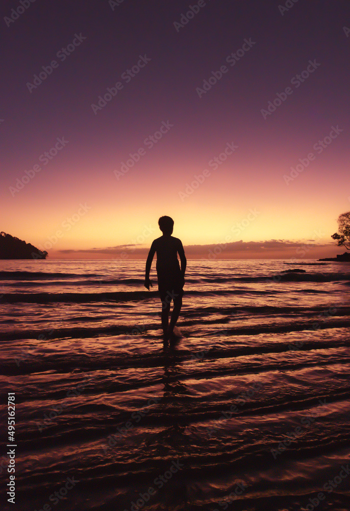 Silhouette of boy standing in shallow water on a beach at sunset. Silhouette of boy standing in shallow water on a beach at sunset.