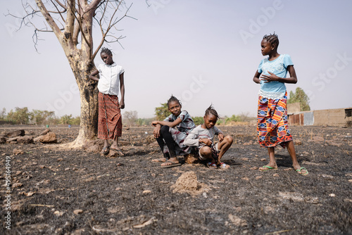 Group of bored young African girls aimlessly hanging around in the arid, desolate landscape of their home village; social issue of demographic growth, neglection, low school attendance or high dropout photo