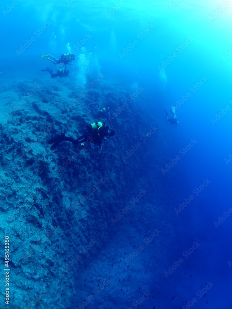 scuba divers around a reef underwater deep blue water big rocks  