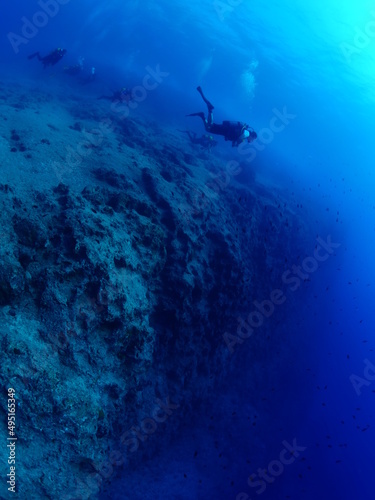 scuba divers around a reef underwater deep blue water big rocks 