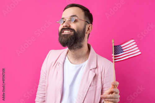 Portrait of a satisfied young man with a beard with an American flag on a red studio background. Great US patriot and defender of freedom.