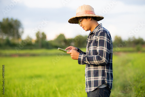 Smart Farmers Concept / Happy young Asian man holding a tablet is checking the rice production that is growing in his farm.