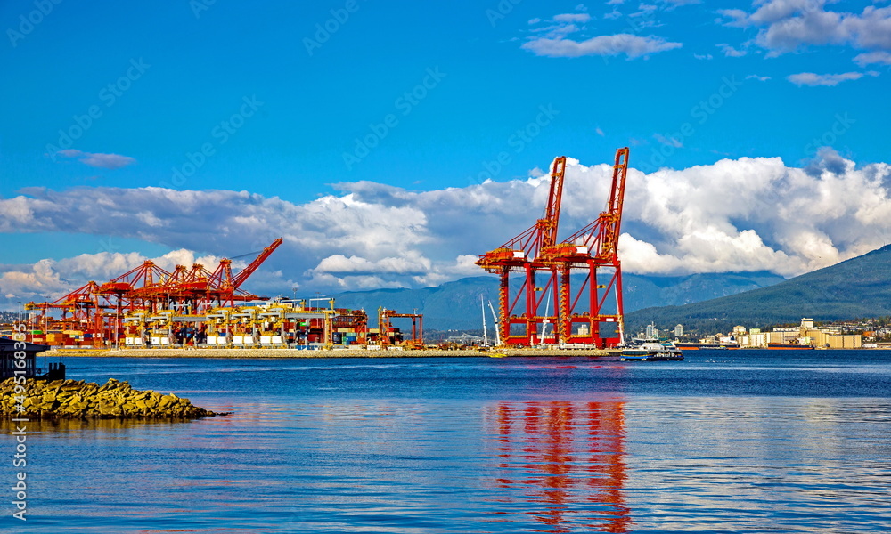 Fototapeta premium Place for loading ocean ships in the seaport of Vancouver, against the backdrop of a blue cloudy sky and a mountain range. North Vancouver at the foot of the mountain range