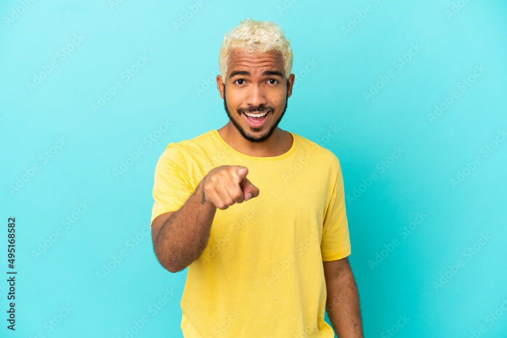 Young Colombian handsome man isolated on blue background surprised and pointing front Young Colombian handsome man isolated on blue background surprised and pointing front