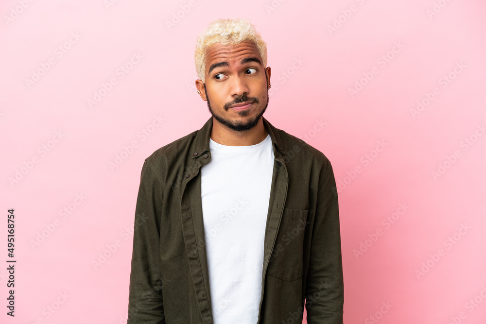 Young Colombian handsome man isolated on pink background making doubts gesture looking side Young Colombian handsome man isolated on pink background making doubts gesture looking side