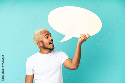 Young Colombian handsome man isolated on blue background holding an empty speech bubble