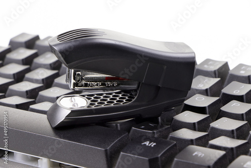 An office stapler and computer keyboard isolated on a white background. A Black plastic stapler. Office supplies