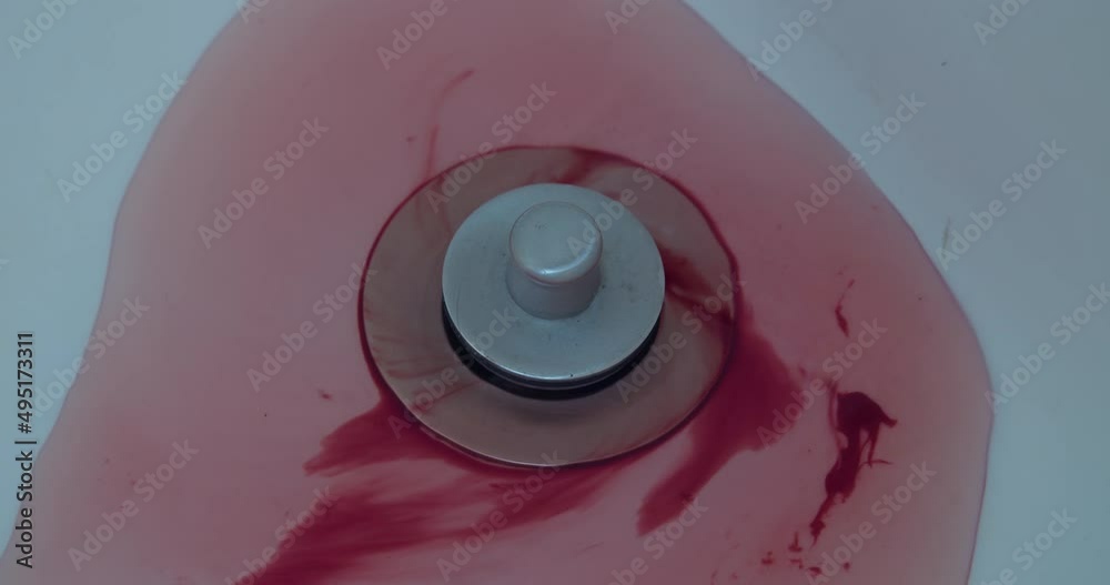 Close-up of blood and water washing down a shower drain.