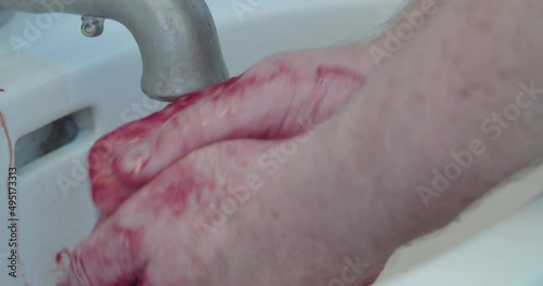 Close-up of a man washing blood off his hands in a bathroom sink.