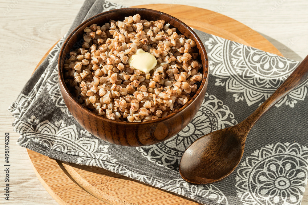 In a wooden bowl, freshly brewed delicious healthy buckwheat porridge with butter for breakfast on a linen napkin with a spoon. In a wooden bowl, freshly brewed delicious healthy buckwheat porridge with butter for breakfast on a linen napkin with a spoon.