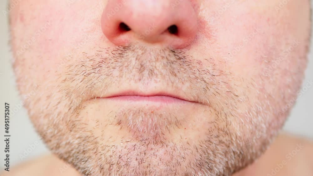 A man examines his regrown stubble, mustache, beard and cheeks in the bathroom. The face of an unshaven man with brown and gray hair. A barber shop client needs grooming and shave. Face care. Close-up