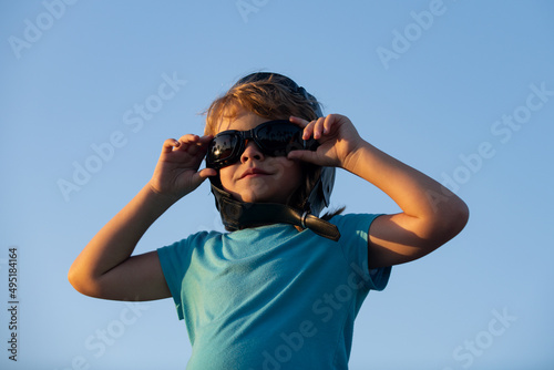 Little boy with pilot goggles and helmet, boy wants to become pilot and astronaut. Happy child play on sky. Kids pilot dreams of flying.