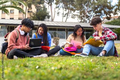 Multiracial college students study together sitting on campus grass using laptop.