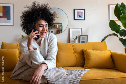 Smiling, happy African American woman talking in mobile phone call relaxing at home sitting in living room couch.