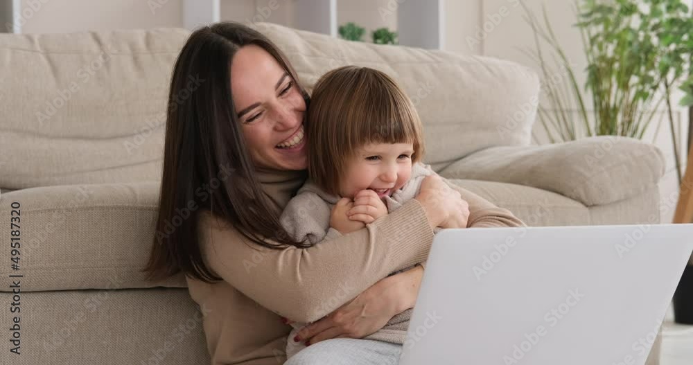 Playful mother tickling daughter while using laptop at home Playful mother tickling daughter while using laptop at home