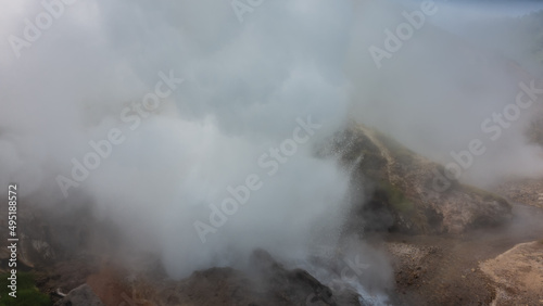 A geyser erupts on the mountainside. There are drops of hot water in the air, clouds of thick steam. Poor visibility. Kamchatka. Valley of Geysers