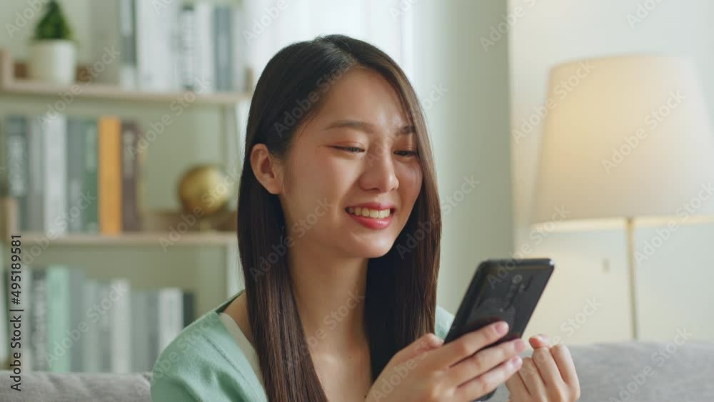 Excited young Asian woman using smartphone showing winner gesture, glad, excite at home Excited young Asian woman using smartphone showing winner gesture, glad, excite at home