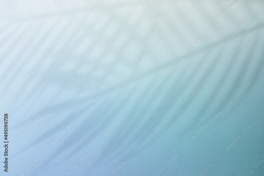 Natural palm leaves shadow on gradient paper background. Abstract blue and mint tropical backdrop. Soft light