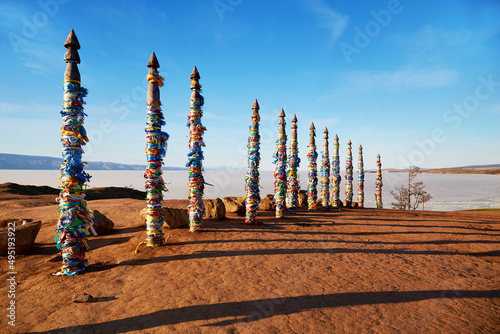 Wooden ritual pillars with multicolored ribbons on Cape Burkhan or Shamanka Rock. Lake Baikal on a sunny spring day, Olkhon Island. The time of ice melting. photo