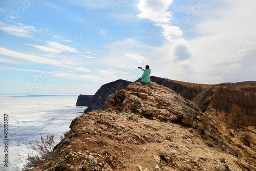 Lake Baikal in spring. A woman sits on a rock and takes photos of beautiful views of white ice floes melting in the water. North of Olkhon Island, Cape Khoboy.