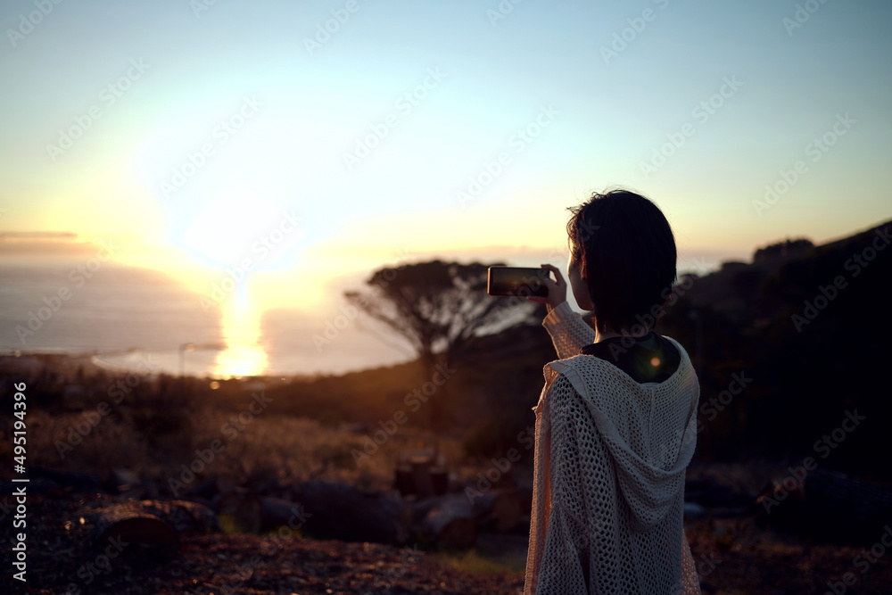 Fototapeta premium I just have to capture this view. Shot of a woman taking pictures on her cellphone of the sunset.