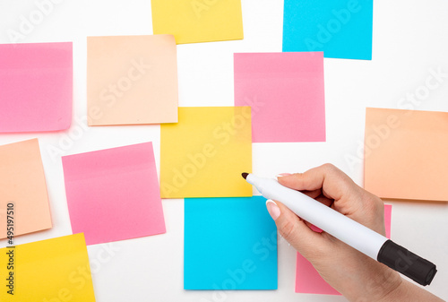 Many colored empty sticker notes on white wall. Business people meeting and use notes to share idea on sticky note. hand with black marker ready to write