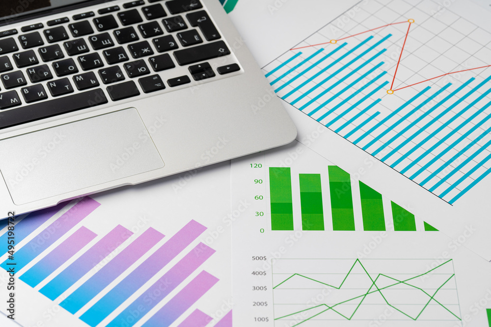 Paper statistics charts and laptop keyboard on white table Paper statistics charts and laptop keyboard on white table