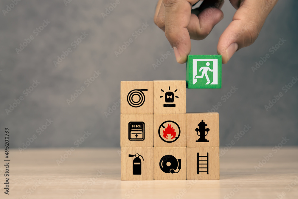 Hand choose wooden block stack with door exit sing or fire escape and fire prevent icon with fire extinguisher and emergency protection symbol for safety and rescue in the building. Hand choose wooden block stack with door exit sing or fire escape and fire prevent icon with fire extinguisher and emergency protection symbol for safety and rescue in the building.