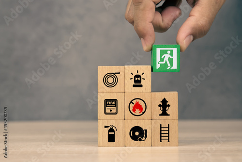 Fotografia, Obraz Hand choose wooden block stack with door exit sing or fire escape and fire prevent icon with fire extinguisher and emergency protection symbol for safety and rescue in the building